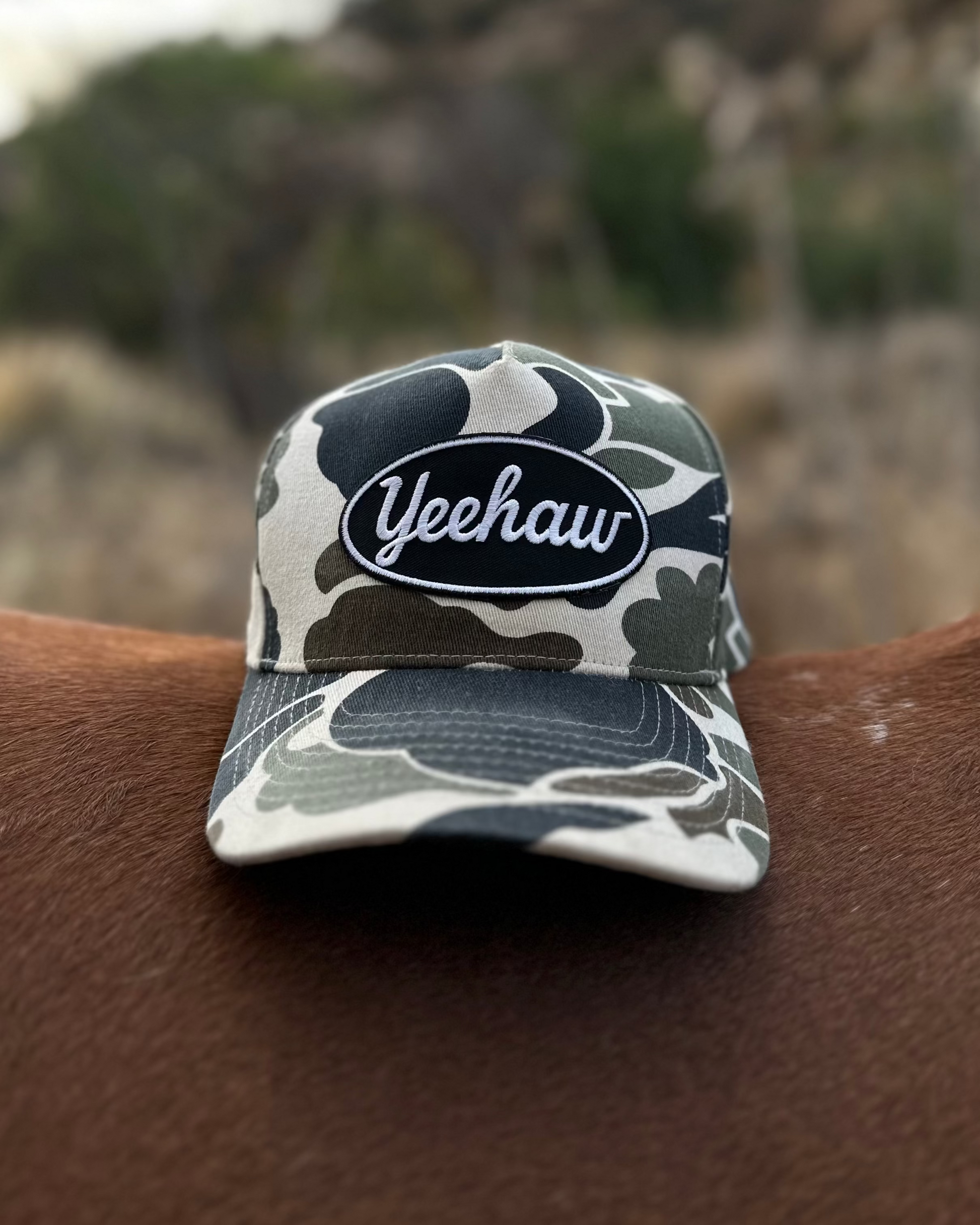 Camouflage-patterned cap with 'Yeehaw' text on a horse's back against a mountainous background